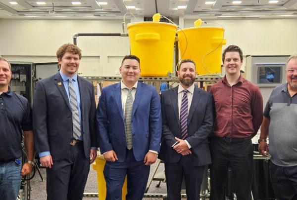 UNF Process Skid team members pose in front of their senior design project. From left are Greg Kline of Vega Americas; Daniel Fowler, 电; Adrian Hoover, 机械, 布莱斯色鬼, 机械; Lake Miller, 电; and 澳门足彩app’s Christian Beckman.